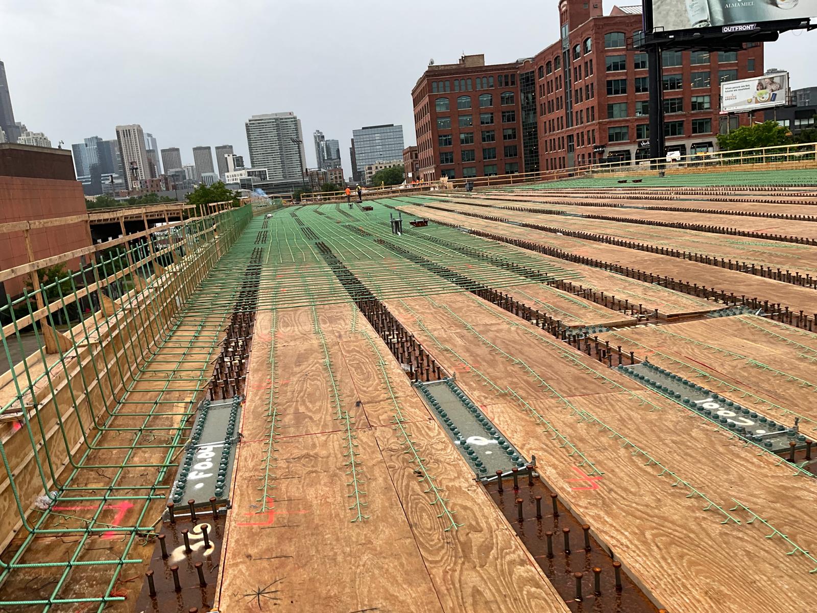 Reinforced concrete bridge deck under construction with the city skyline behind.