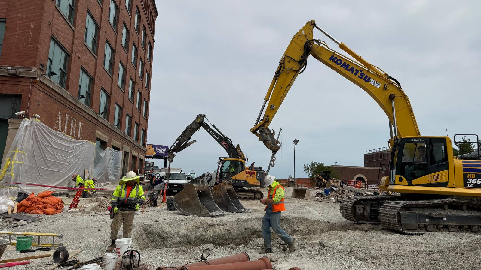 Heavy civil construction site with an excavator, workers, and utilities in progress.