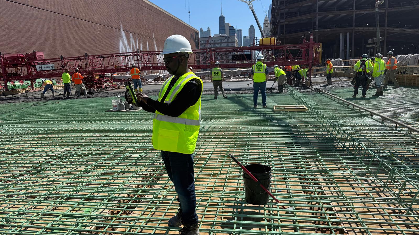CHI-IBANDA engineer in hard hat and safety vest on a reinforced concrete deck with cranes and city skyline
